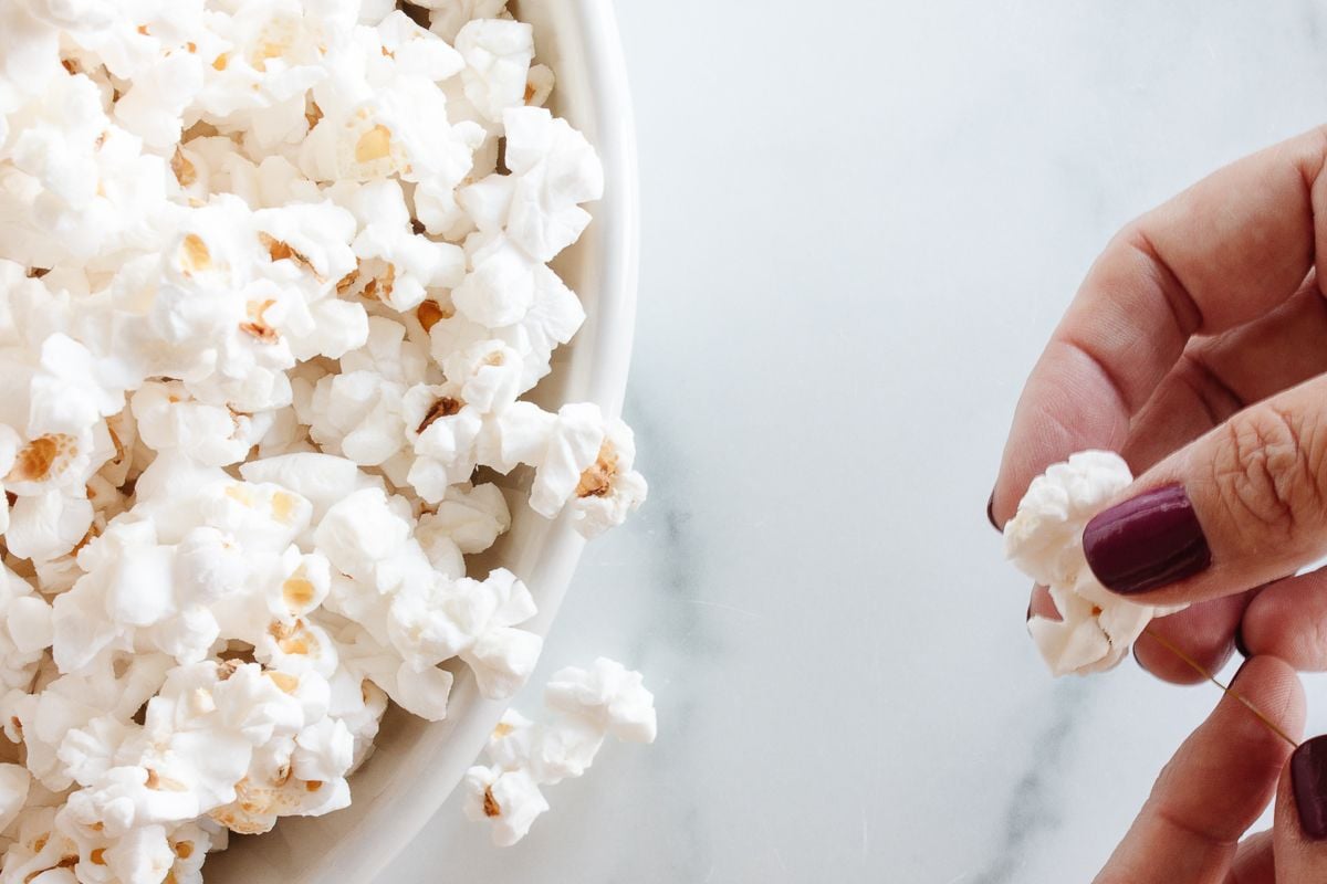 A bowl of popcorn, and a woman's hands showing how to make popcorn garland.