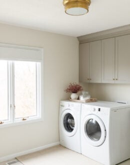 neutral laundry room with gray cabinets and brass light