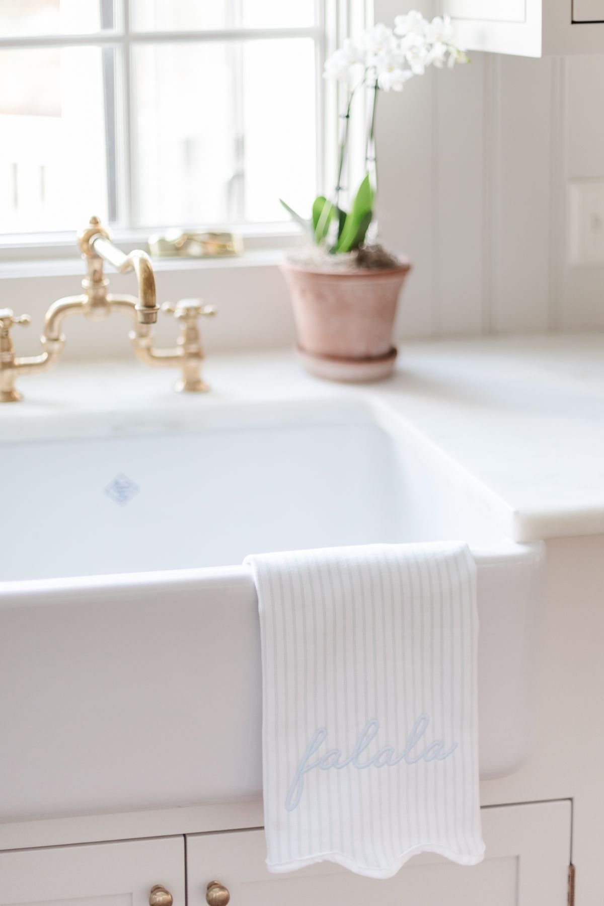 A white kitchen sink decorated with a holiday towel and a potted orchid, for a minimalist Christmas look.