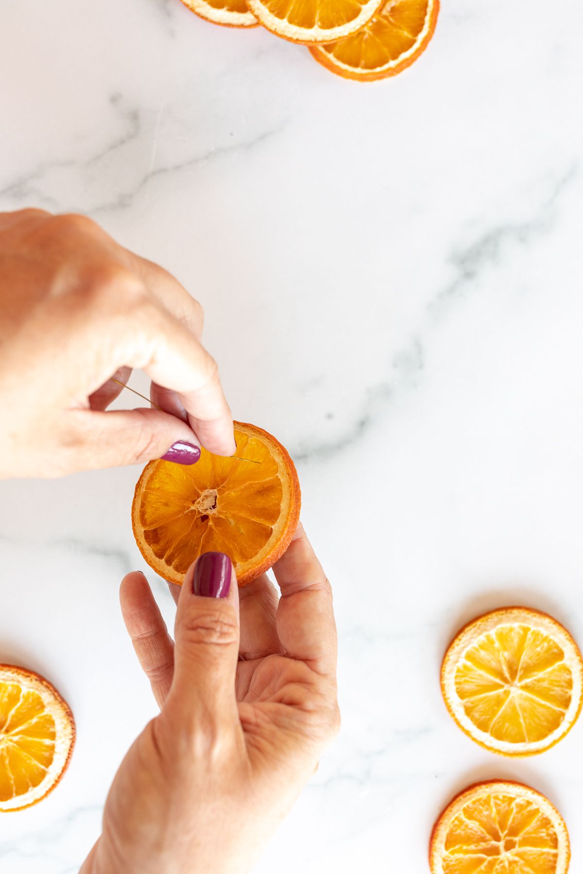 A woman's hands stringing an orange garland on a marble surface.