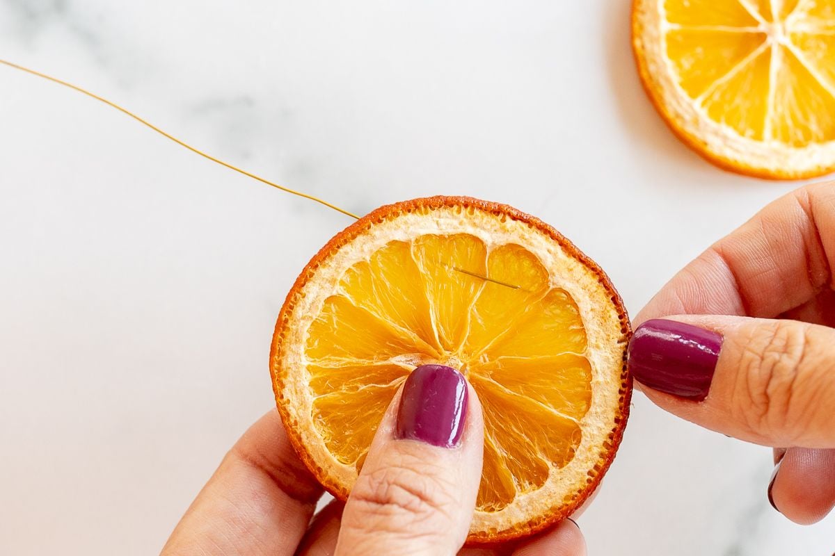 A woman's hands stringing an orange garland on a marble surface.