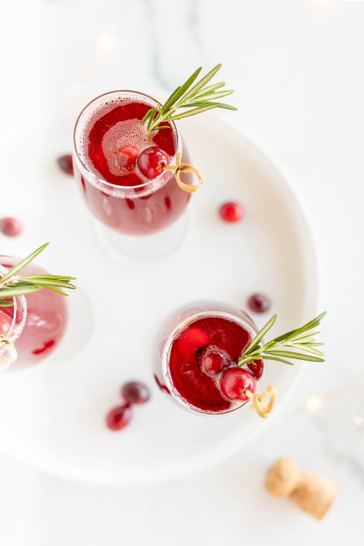 A white tray with 3 glasses full of a poinsettia cocktail, cranberry and rosemary garnish