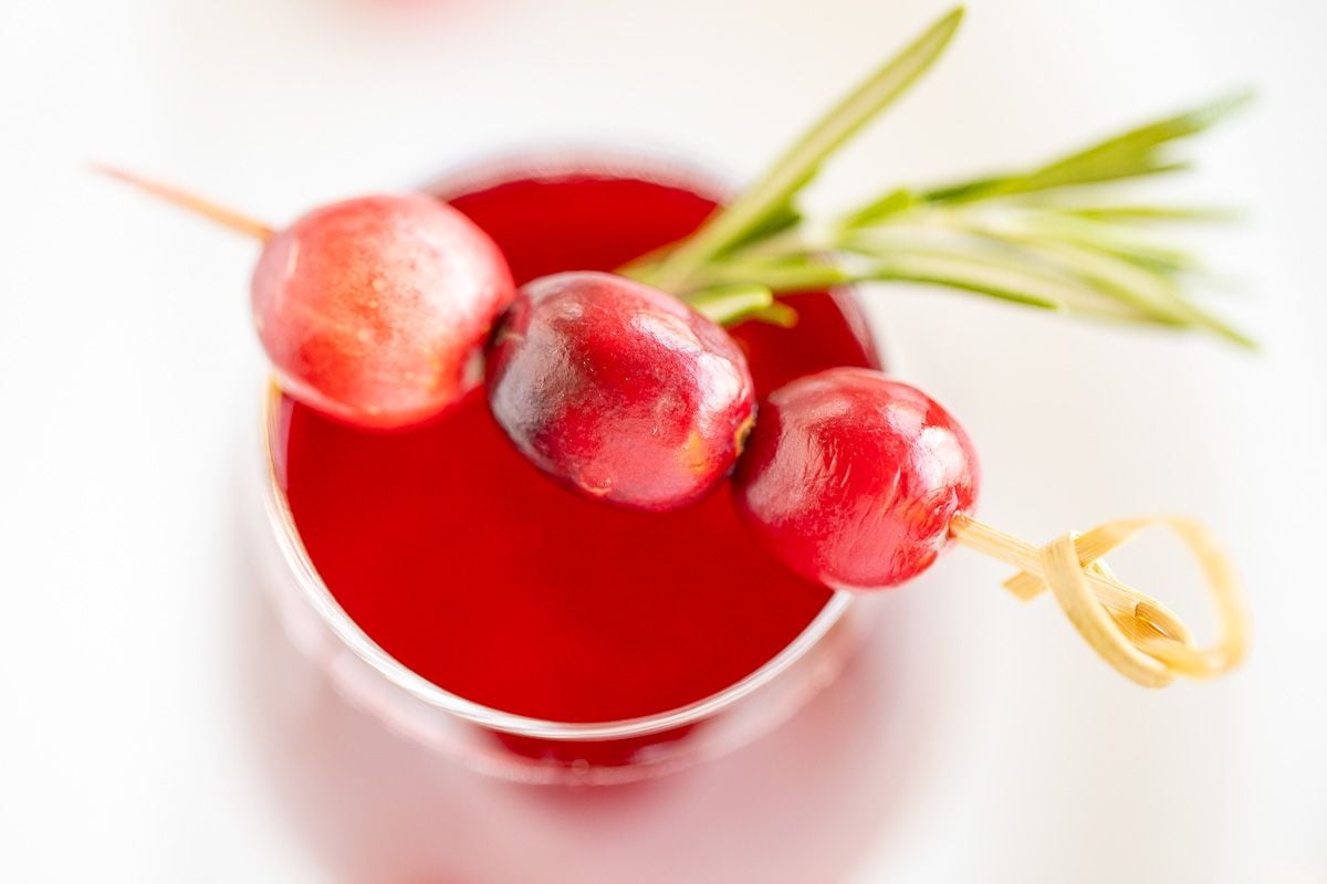 A glass full of a champagne poinsettia cocktail for Christmas, cranberry and rosemary garnish!