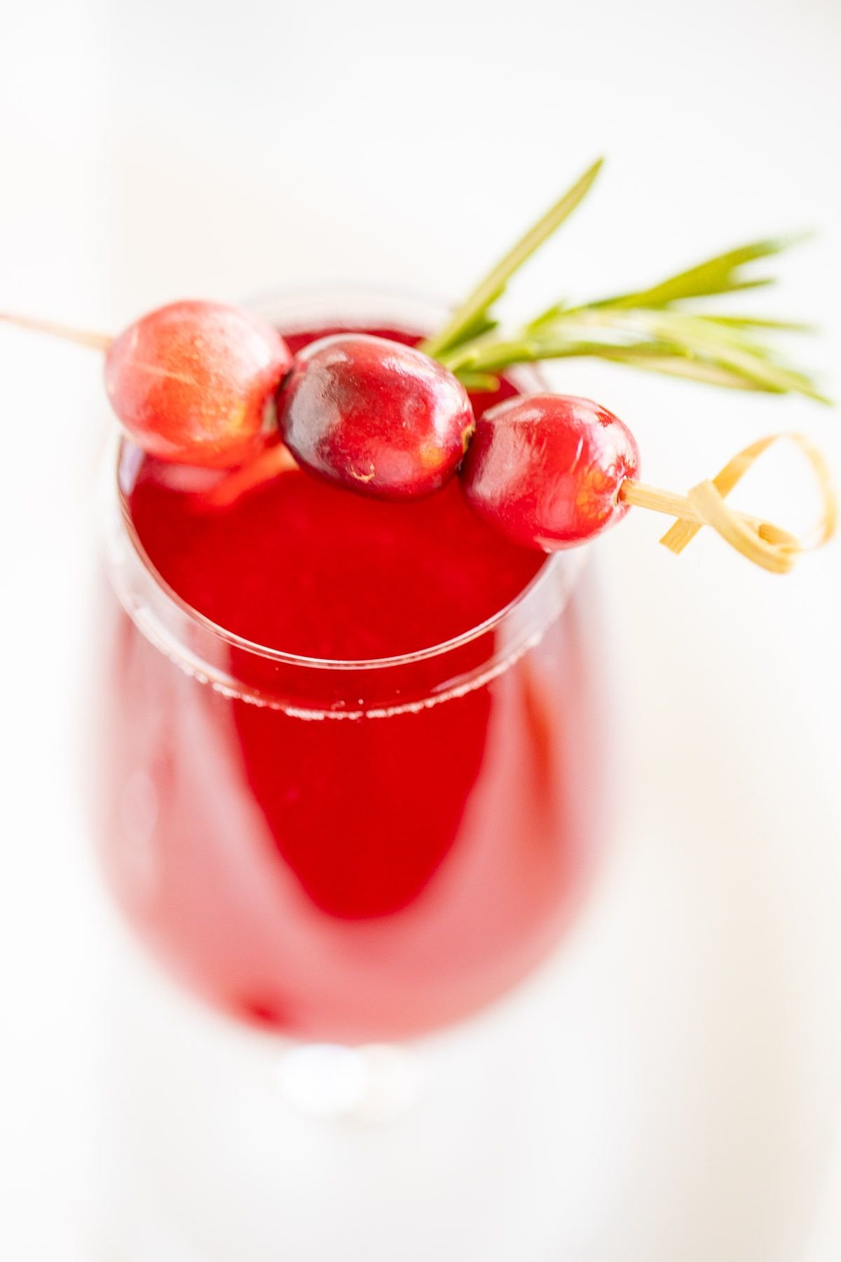 A glass full of a champagne poinsettia cocktail for Christmas, cranberry and rosemary garnish!