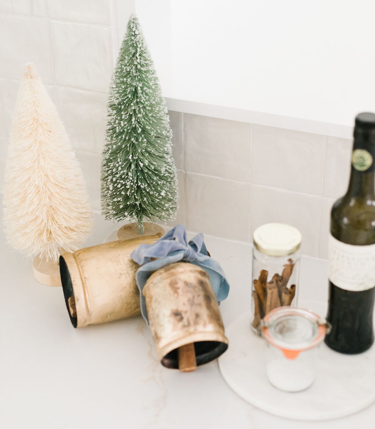 A Christmas display of brass bells and bottle brush trees on a kitchen counter