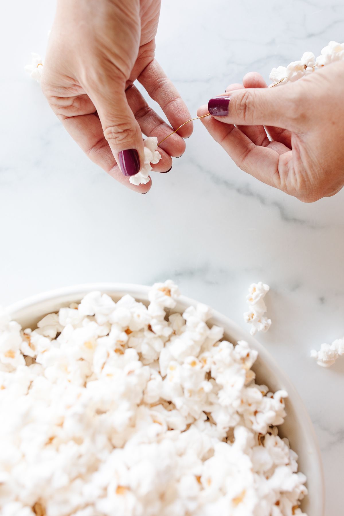 A bowl of popcorn, and a woman's hands showing how to make popcorn garland.