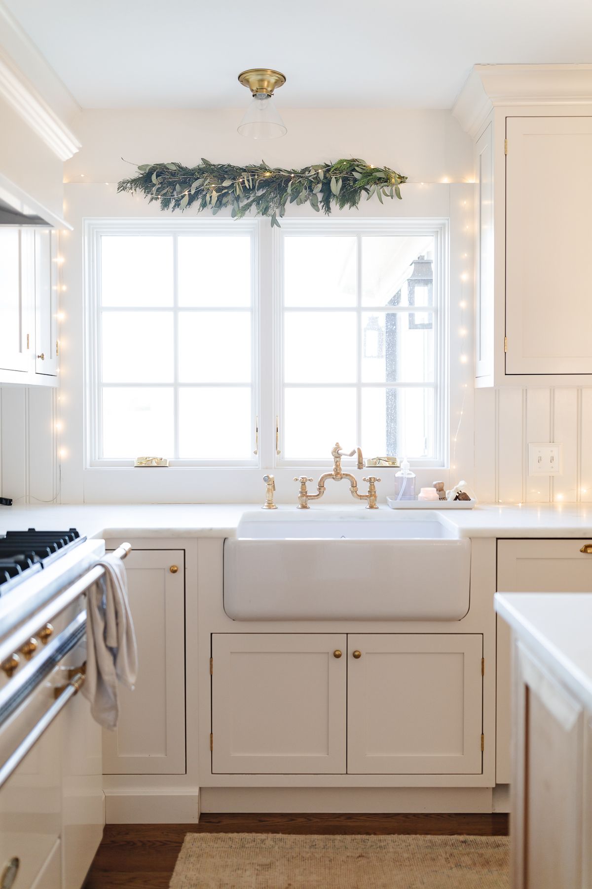 A greenery garland over a kitchen sink window in a white kitchen