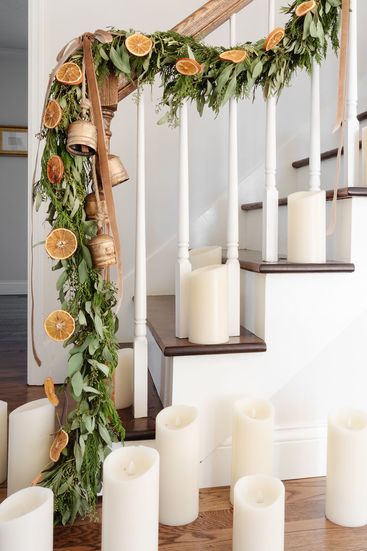 An orange garland on a staircase with evergreen garland, velvet ribbon and brass bells.