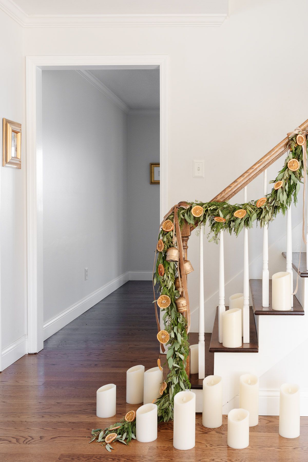 An orange garland on a staircase with evergreen garland, velvet ribbon and brass bells.