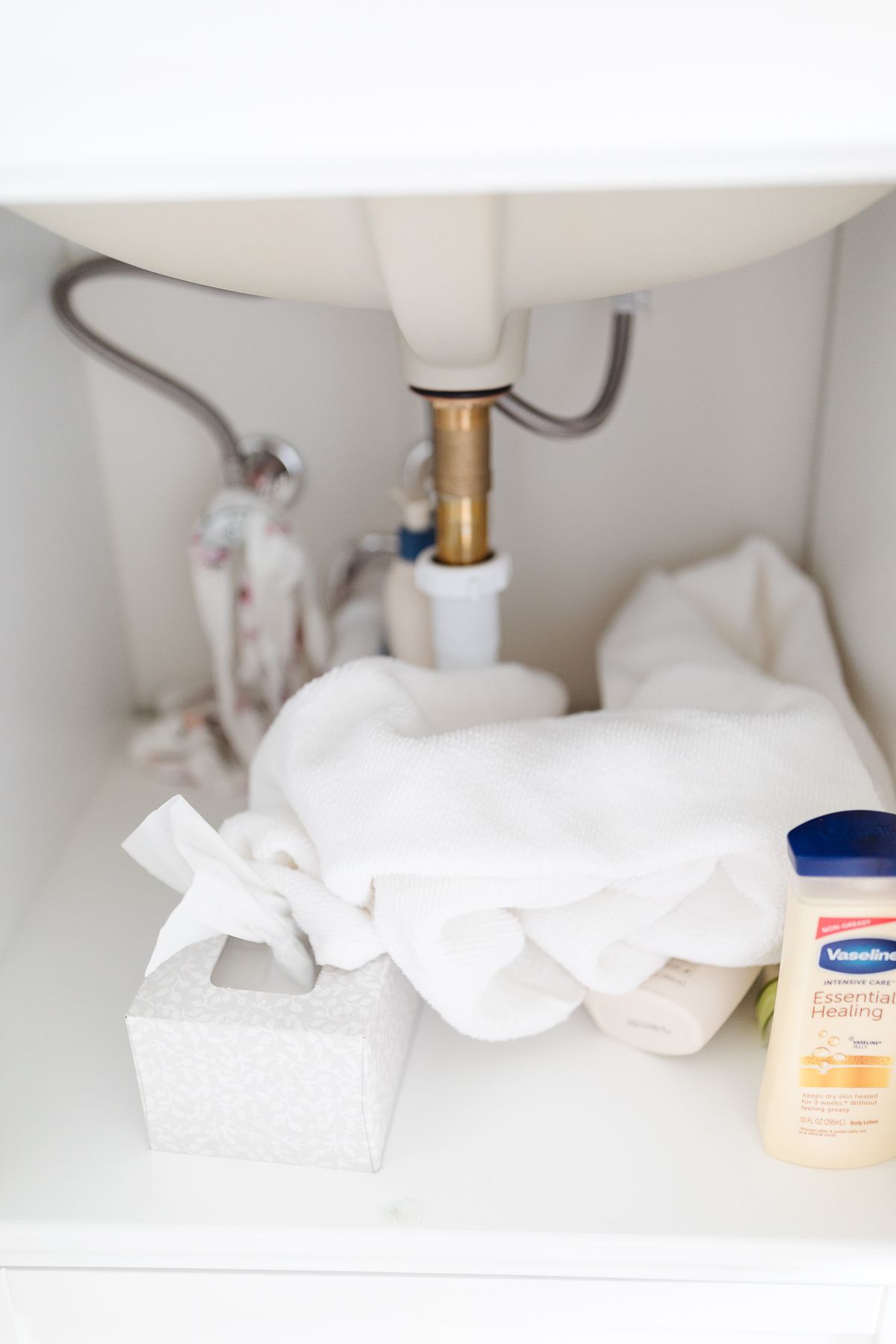 A bathroom cabinet under a sink with messy towels and no organization