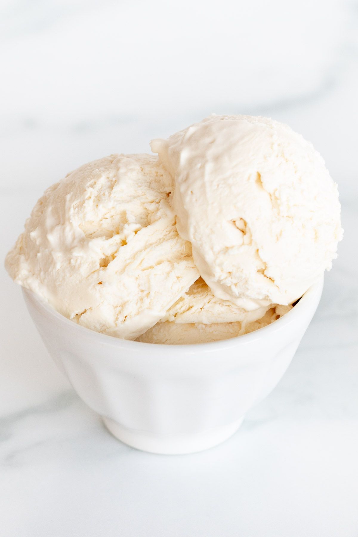 A white bowl on a marble surface, filled with frozen mascarpone ice cream