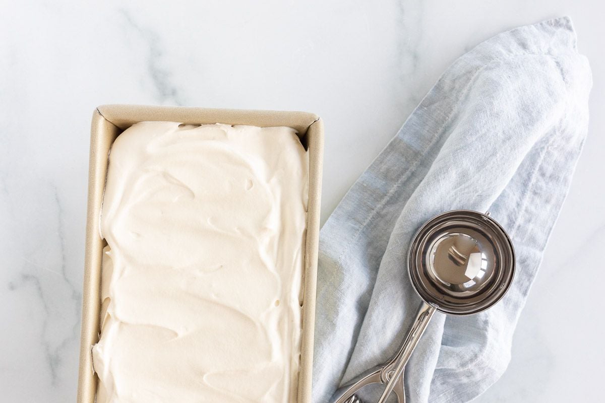 A gold loaf pan filled with homemade mascarpone ice cream, scoop to the side