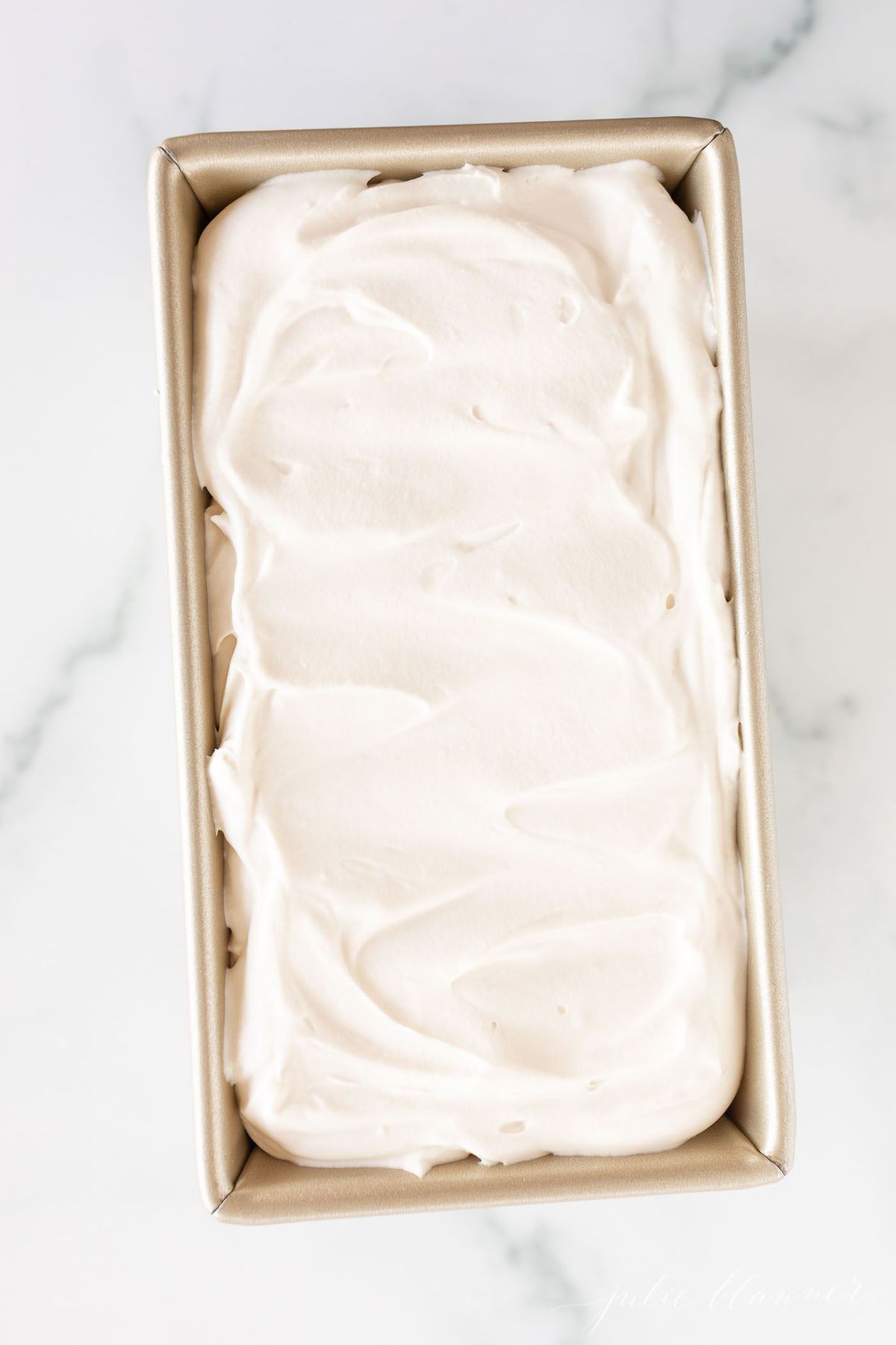 A gold loaf pan rests on a marble surface, filled with frozen mascarpone ice cream