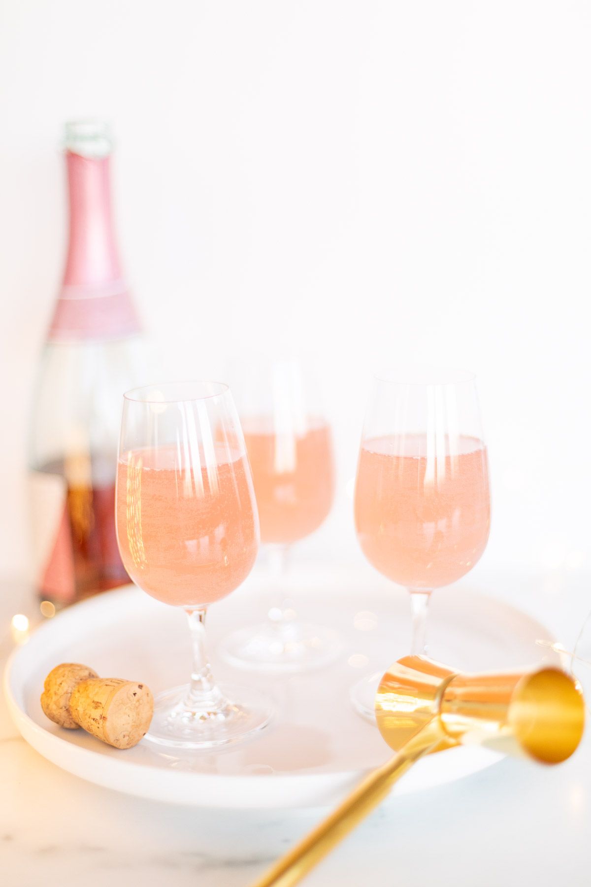 3 glasses of champagne margaritas on a white tray, gold confetti surrounding and a bottle of pink champagne in the background