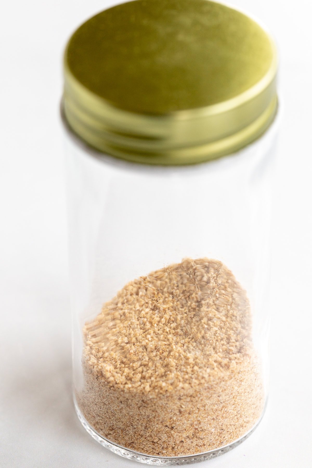 A clear glass jar with a gold lid contains a small amount of ground sesame seeds, perfect for adding to your favorite dishes or blending with beau monde seasoning.