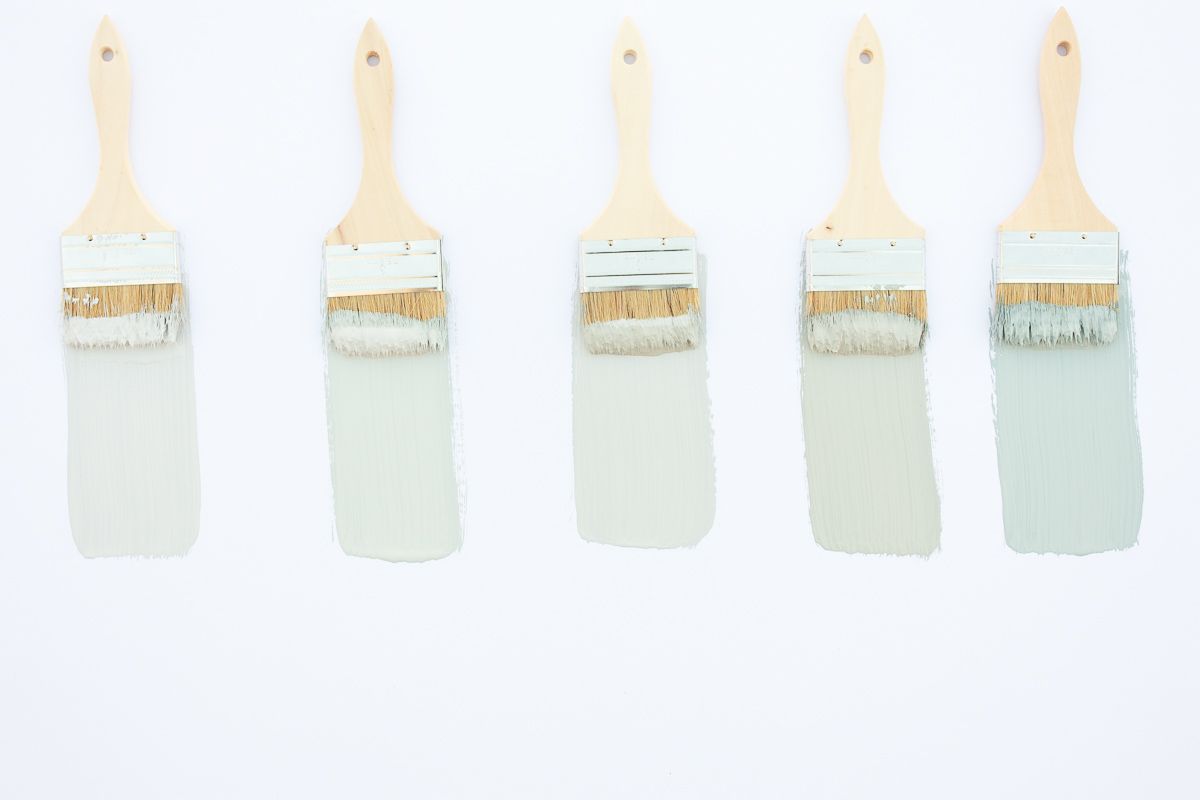 5 paint brushes laid out on a white surface, with samples of blue gray paint colors