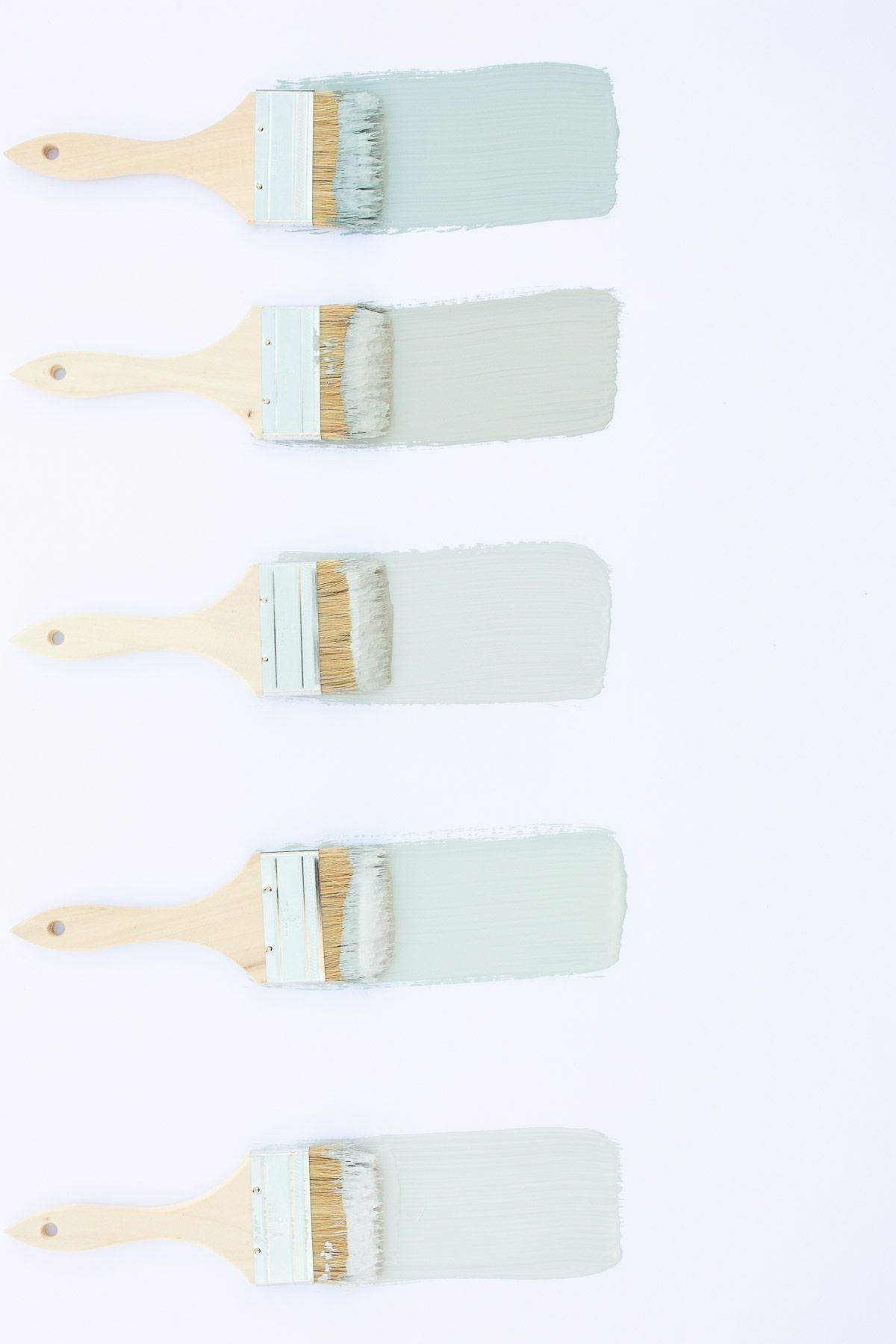 5 paint brushes laid out on a white surface, with samples of blue gray paint colors