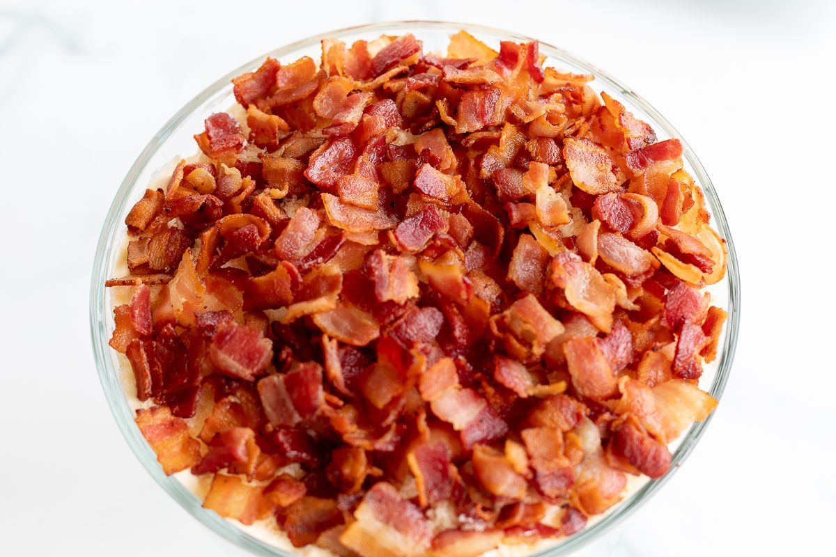 A clear glass bowl of salad topped with chopped bacon