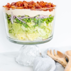 Seven layer salad topped with bacon on a marble countertop