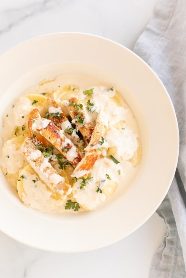 Tortelloni alfredo with grilled chicken on a white plate.