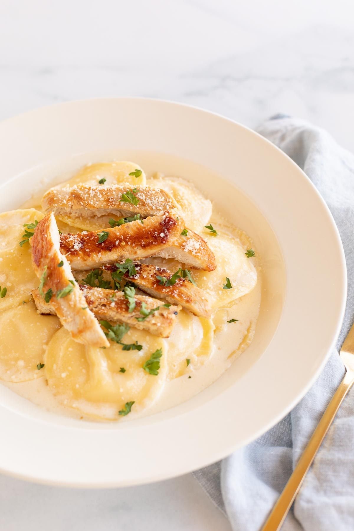 Tortelloni alfredo with grilled chicken on a white plate.