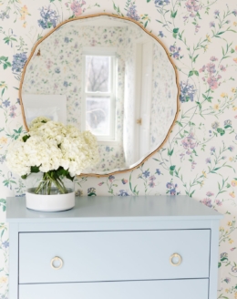 A bedroom with floral wallpaper and a dresser painted in a slate Blue color