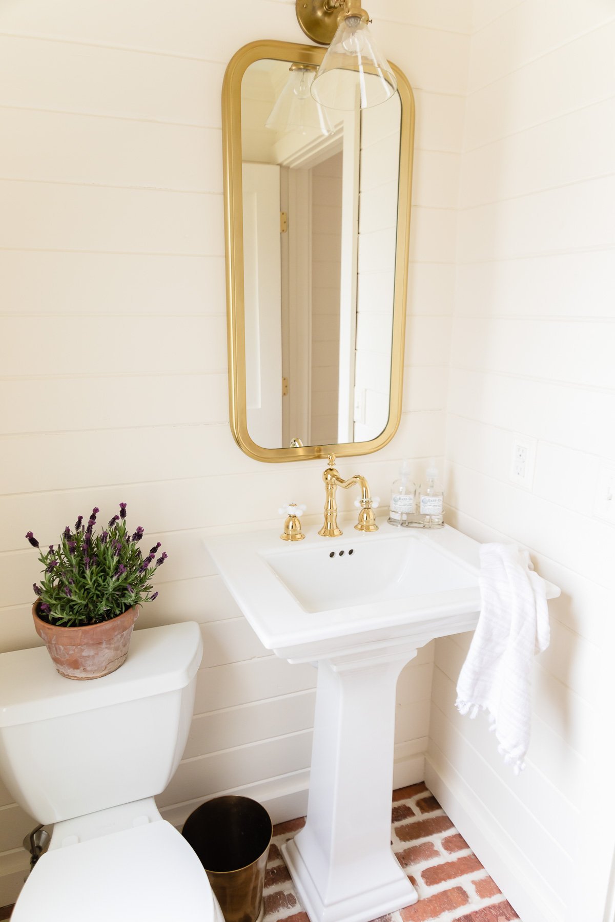 A bathroom with brick floors and shiplap walls with a cream paint color. 