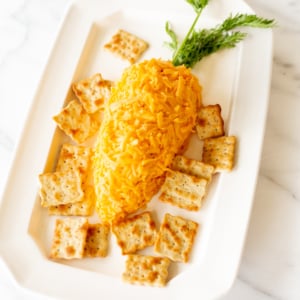 One of the best Easter recipes, a carrot shaped Easter cheese ball, surrounded by crackers on a white platter.