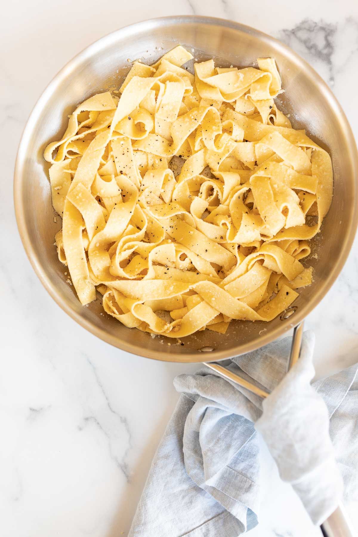 A silver sauce pan on a marble counter, filled with pasta in a garlic parmesan sauce