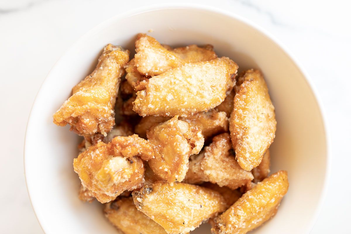 Wings in a white bowl, coated in garlic parmesan sauce