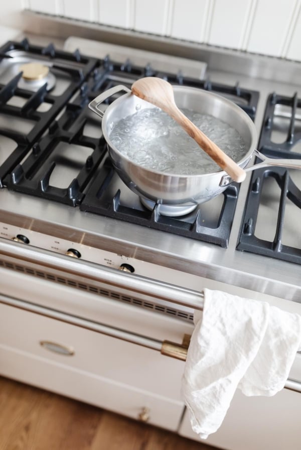 A silver pot of boiling water on a French range, with a wooden spoon placed over the top to stop water from boiling over.