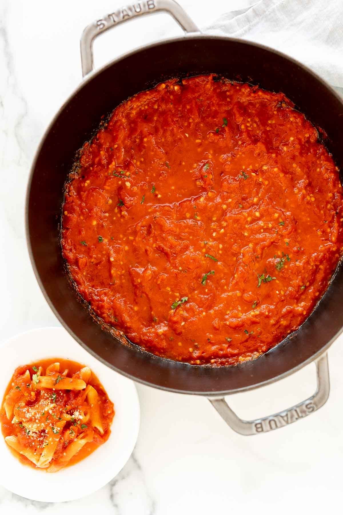 A cast iron pan full of arrabbiata sauce, plated sauce and pasta to the side