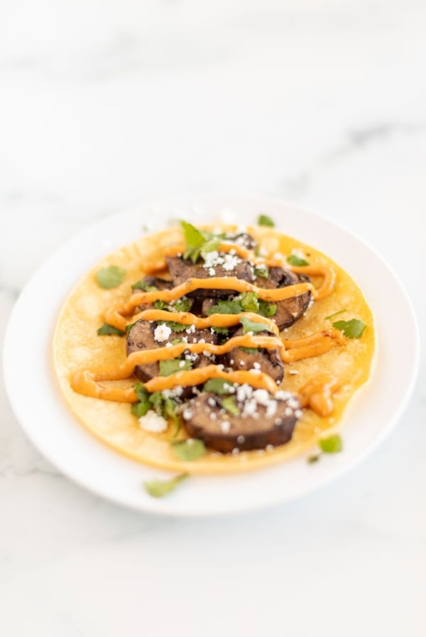 A portobello mushroom taco in a corn tortilla on a white plate