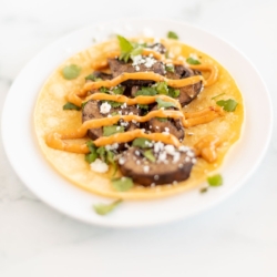 A portobello mushroom taco in a corn tortilla on a white plate