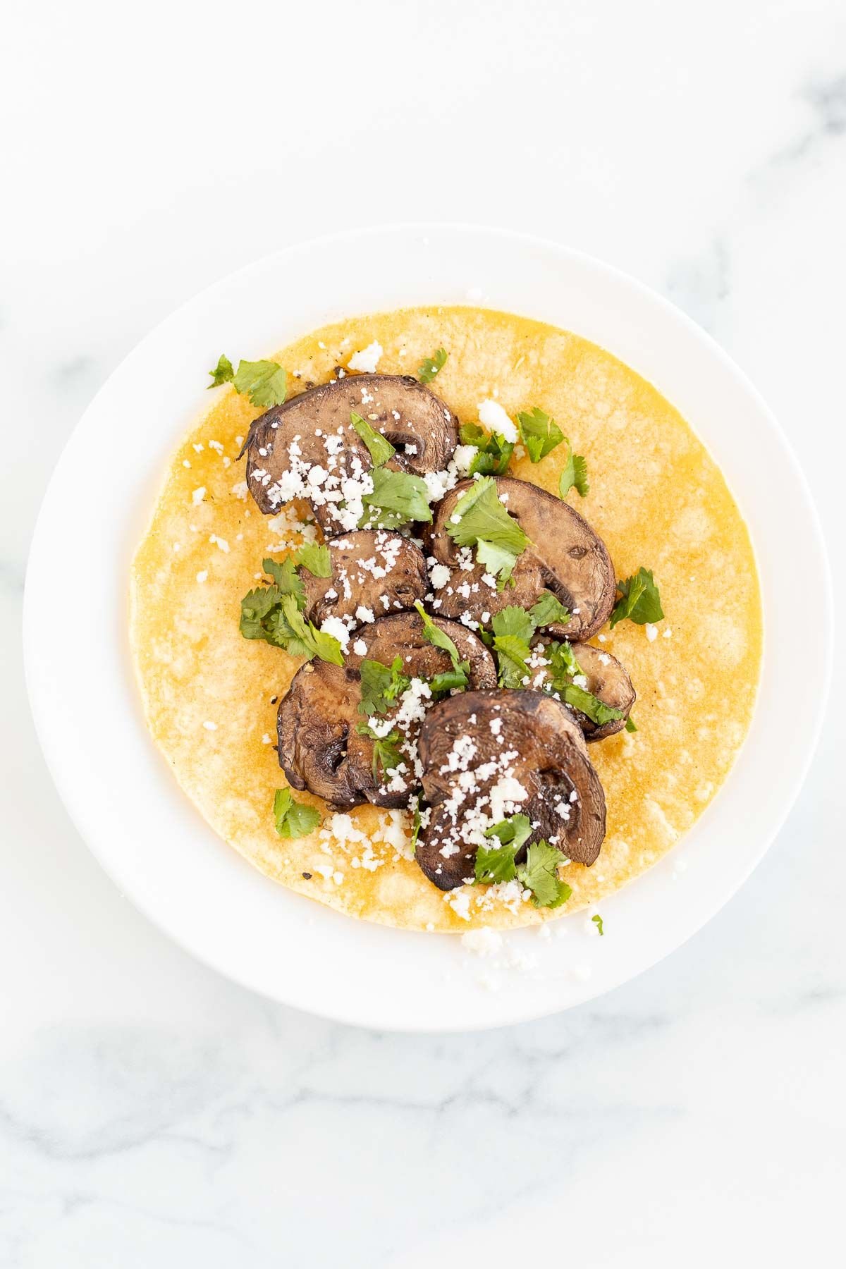 A portobello mushroom taco in a corn tortilla on a white plate
