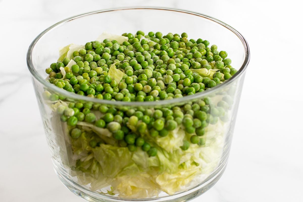 Chopped lettuce topped with peas in a glass serving dish.