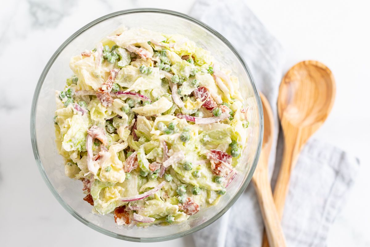 A 7 layer salad mixed up in a glass serving dish, wooden spoons to the side