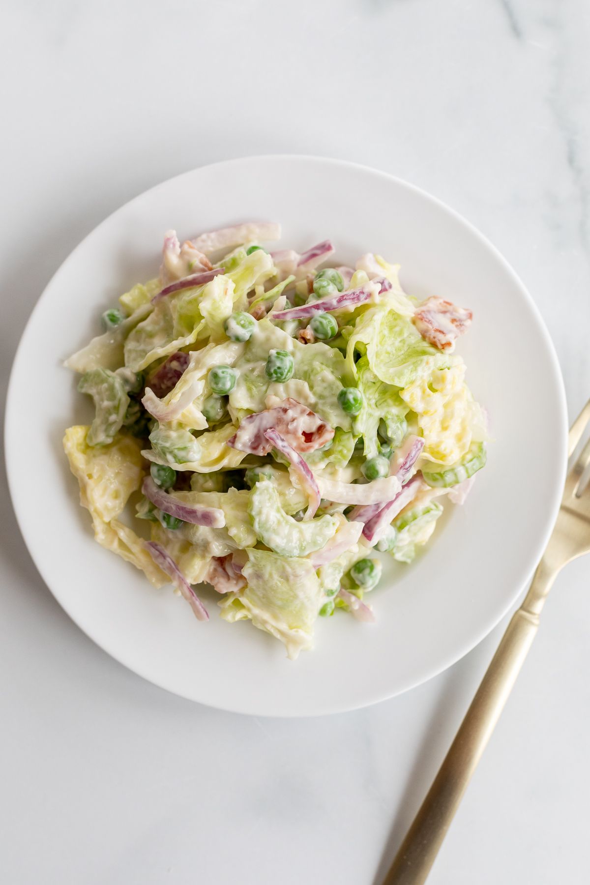 A white plate with a serving of seven layer salad, fork to the side