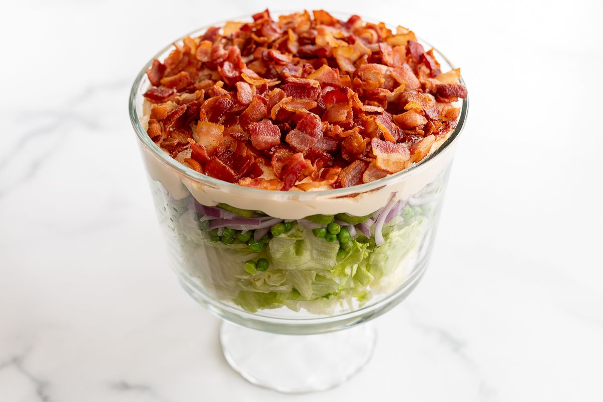 Seven layer salad topped with bacon on a marble countertop