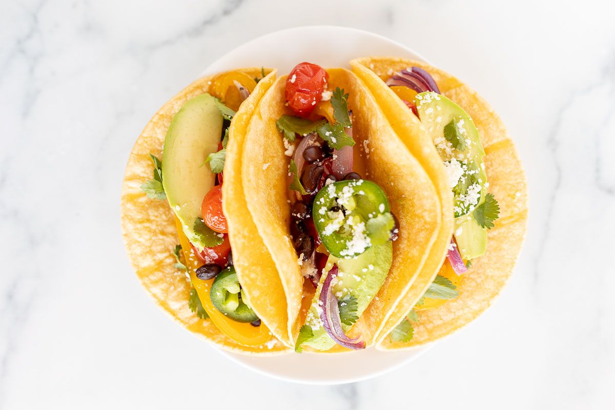 A white plate full of veggie tacos in corn tortillas