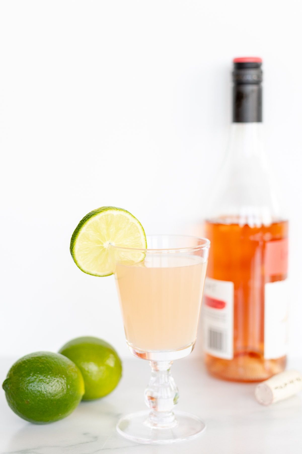 A wine margarita cocktail in a wine glass, garnished with a slice of lime, bottle of wine in background