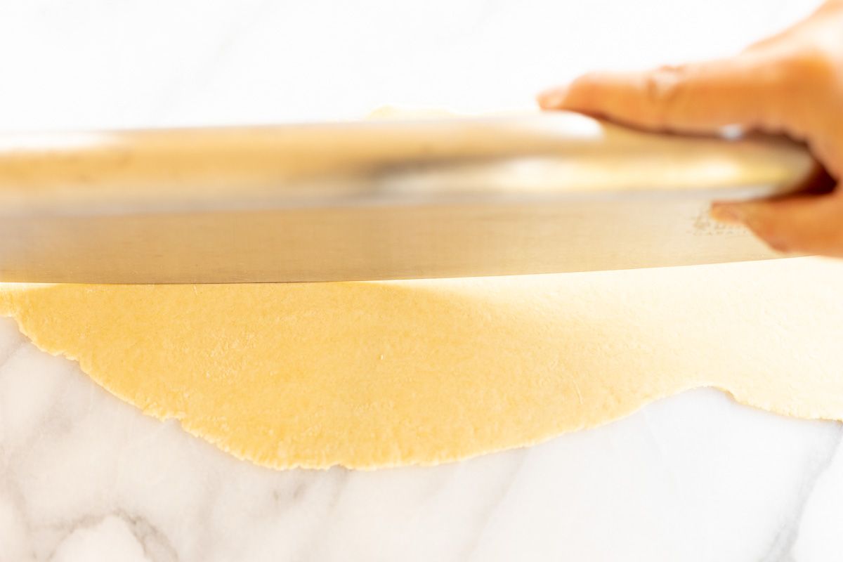 A sheet of homemade pasta dough laid out on a marble surface, cut into strips for Pappardelle