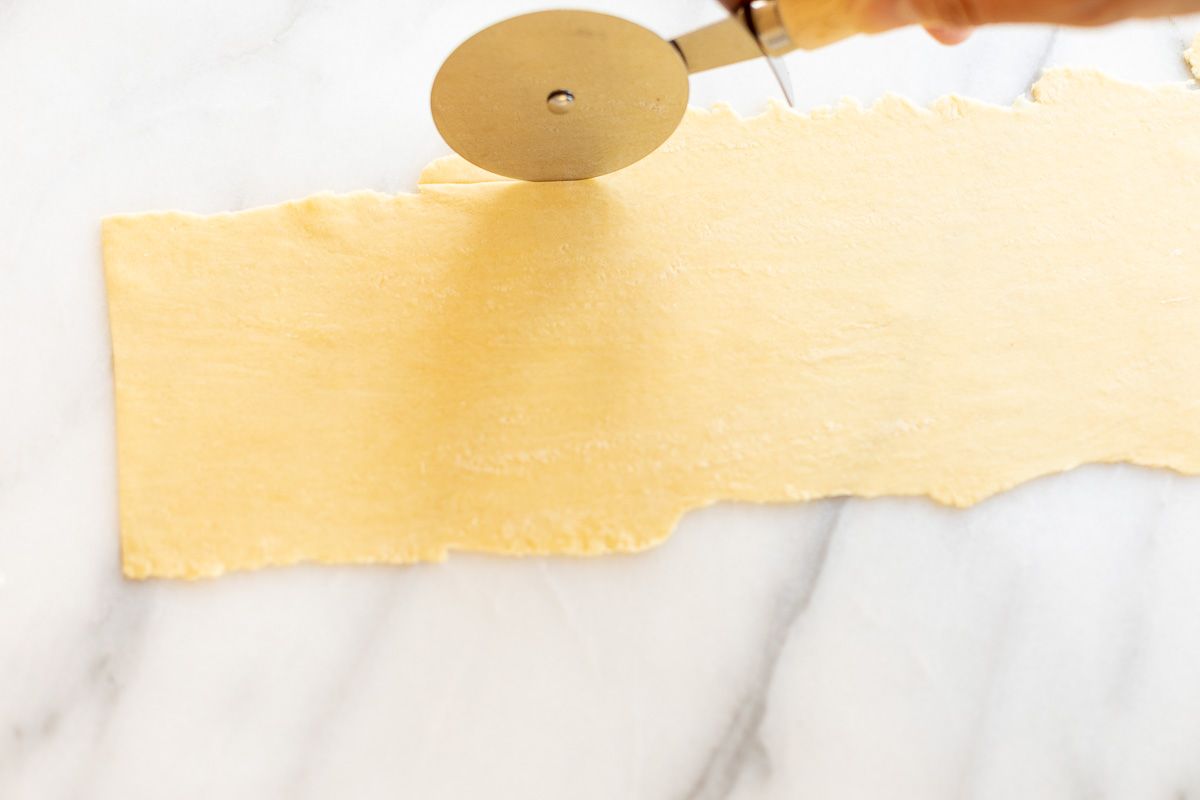 A sheet of homemade pasta dough laid out on a marble surface, cut into strips for Pappardelle