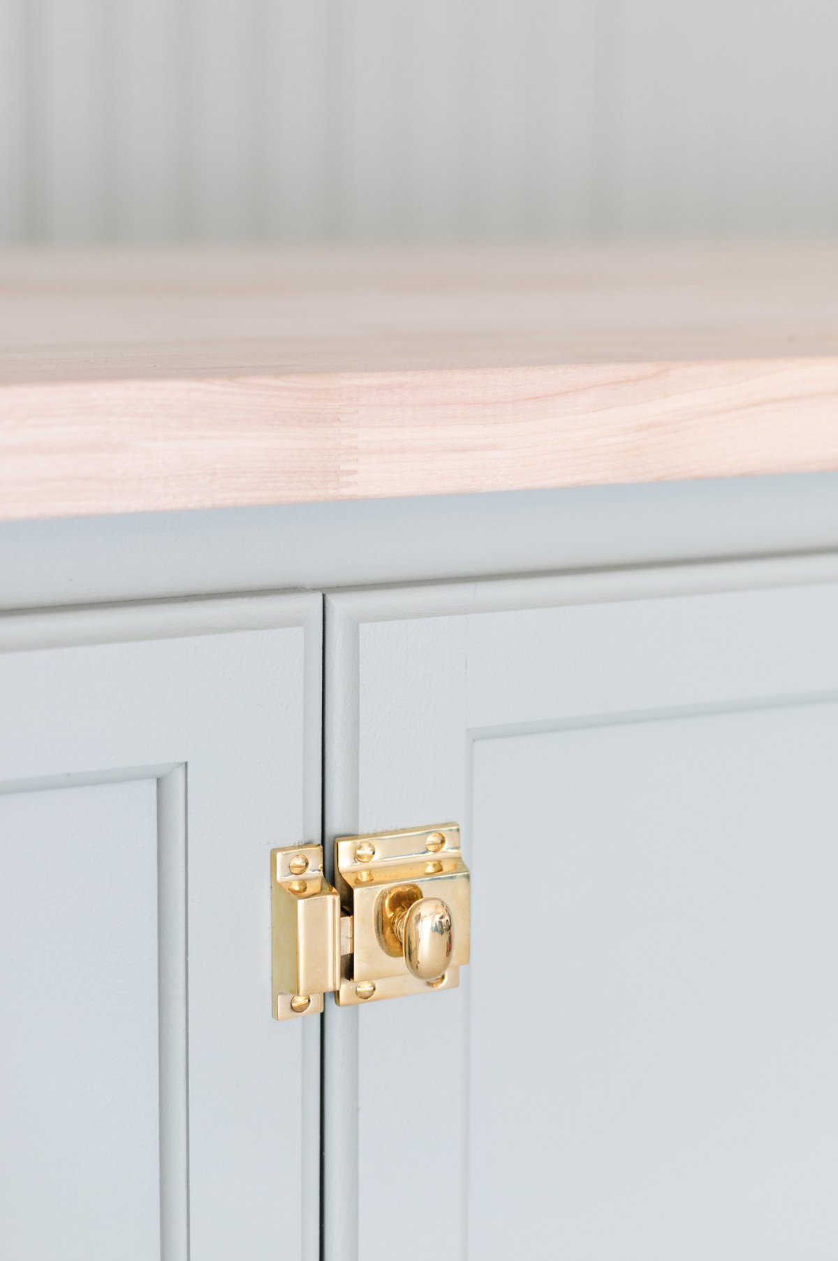 A green potting bench with brass hardware and cabinet latches