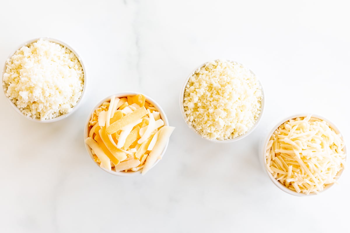 Four bowls of Mexican cheese in white bowls on a marble surface.