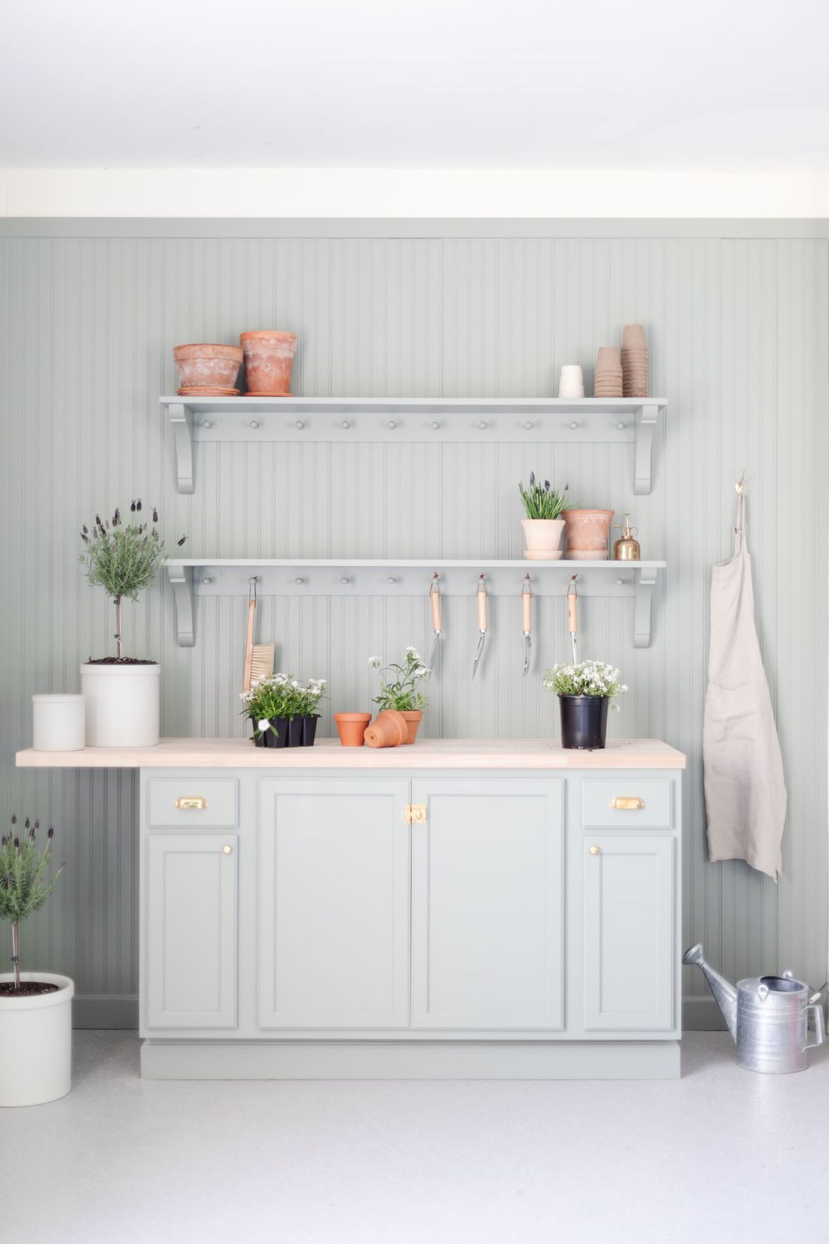 A potting bench painted in a green gray color, flowers and tools on top