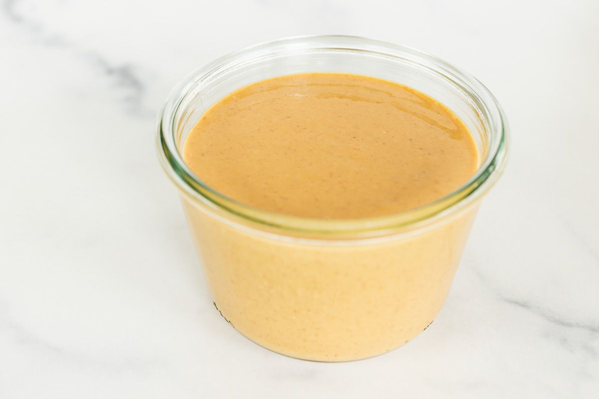 A small glass jar of homemade peanut butter on a marble surface.