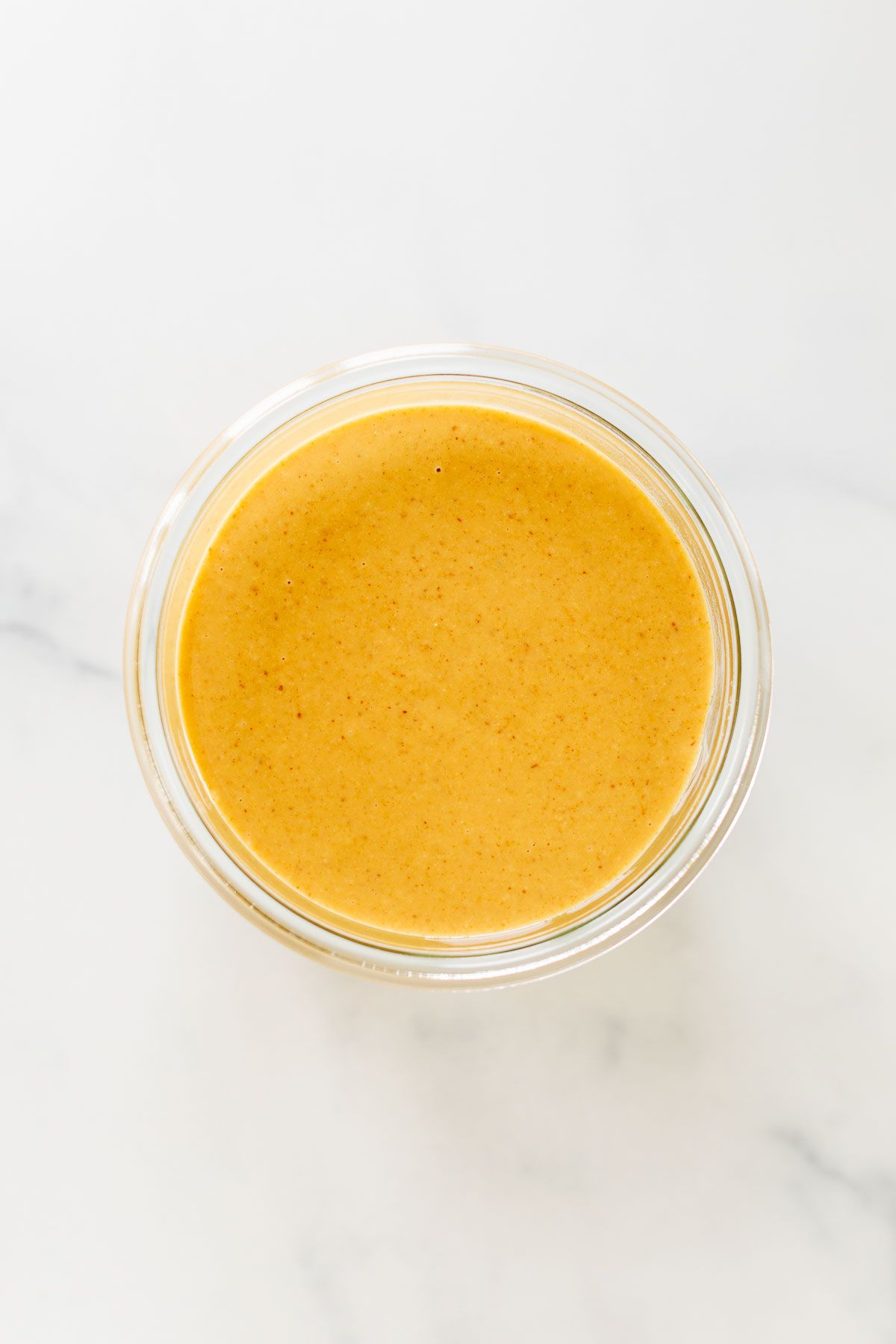 A small glass jar of homemade peanut butter on a marble surface.