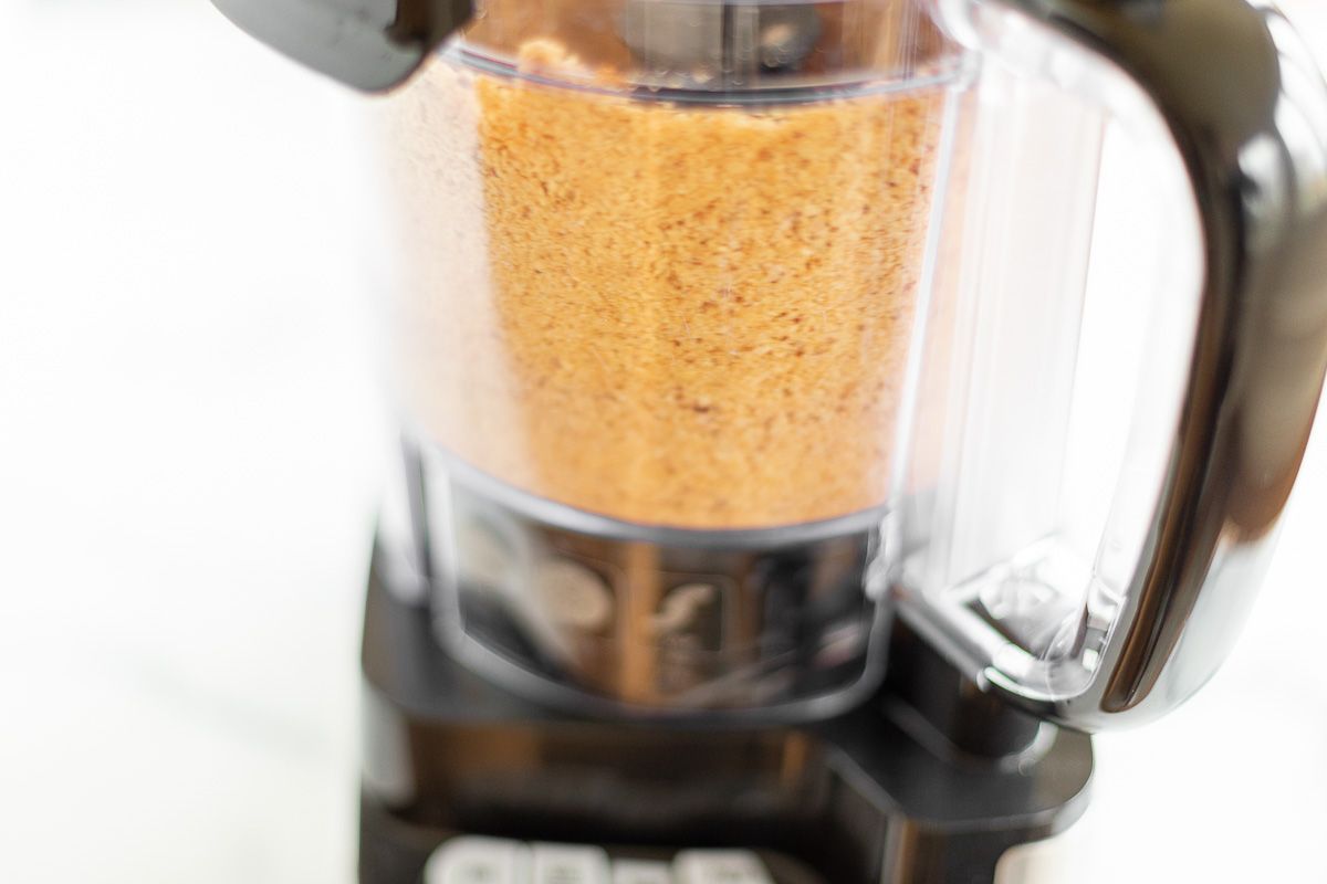 Image features homemade peanut butter in a food processor as part of a tutorial for how to make peanut butter.