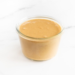 A small glass jar of homemade peanut butter on a marble surface.